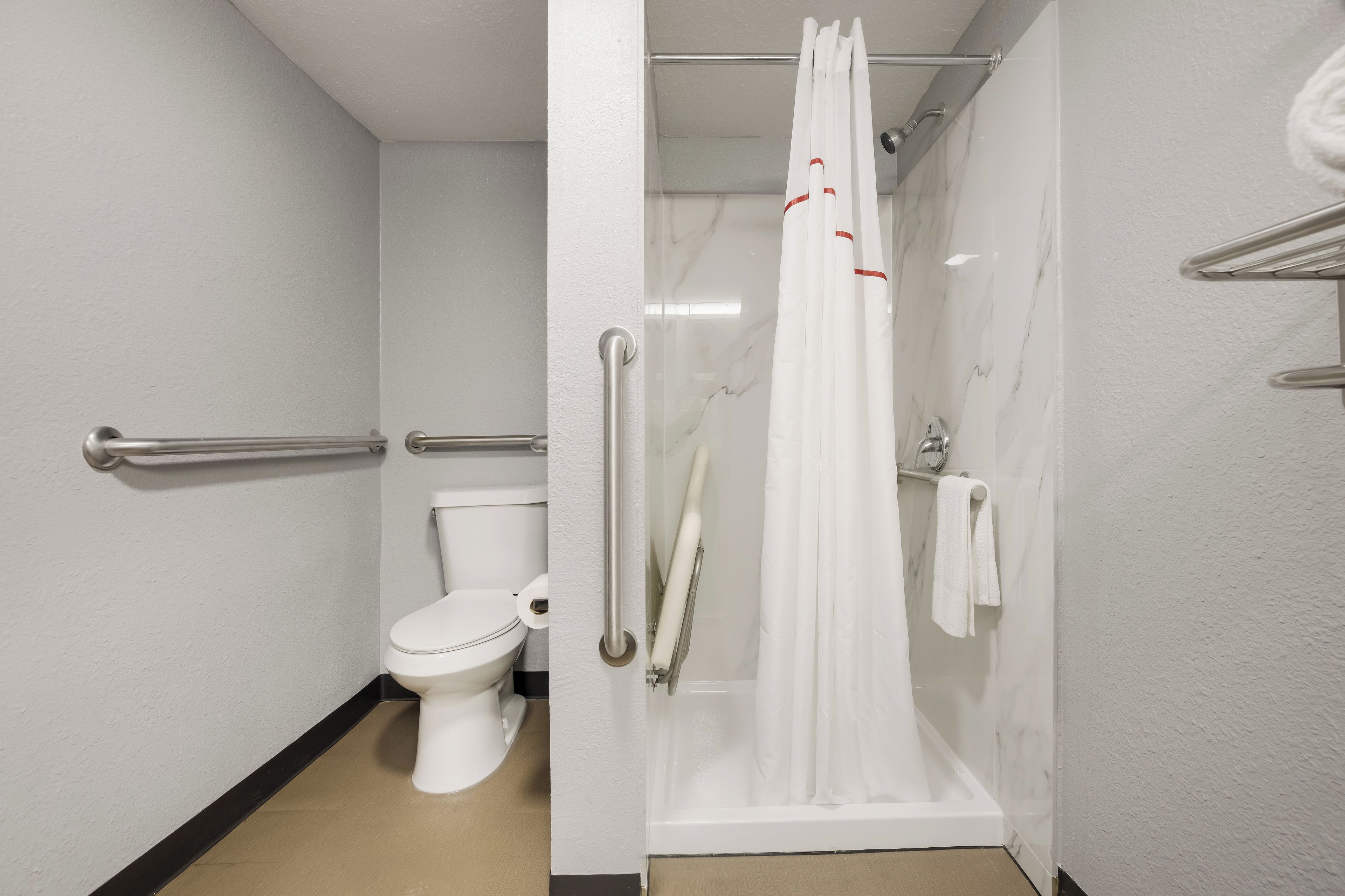 A modern bathroom with a toilet, a shower with a glass door, and a handrail.