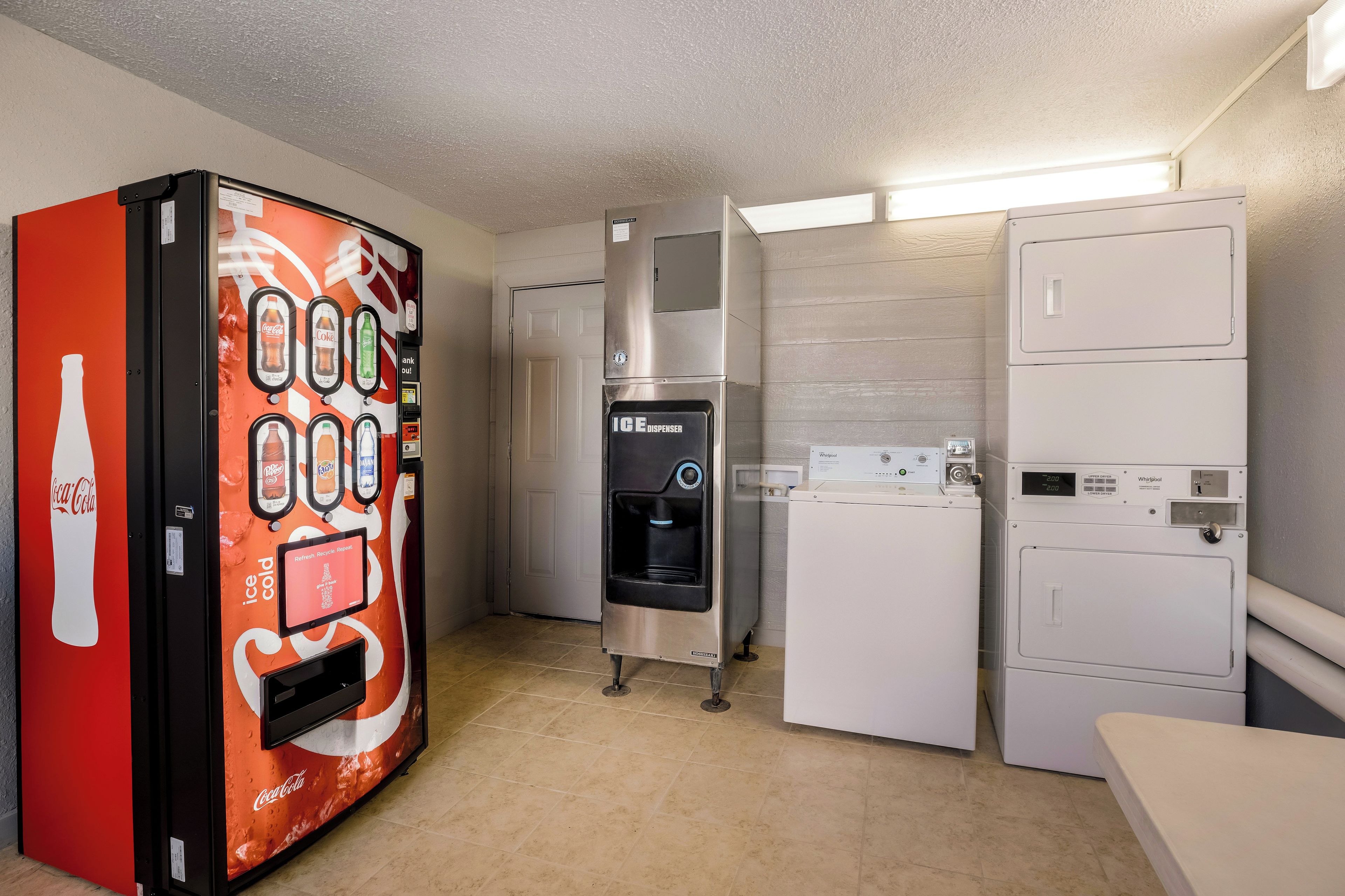 Ein kleines Hotelzimmer mit einem Coca-Cola Automaten, einer Whirlpool Waschmaschine und einem Trockner.