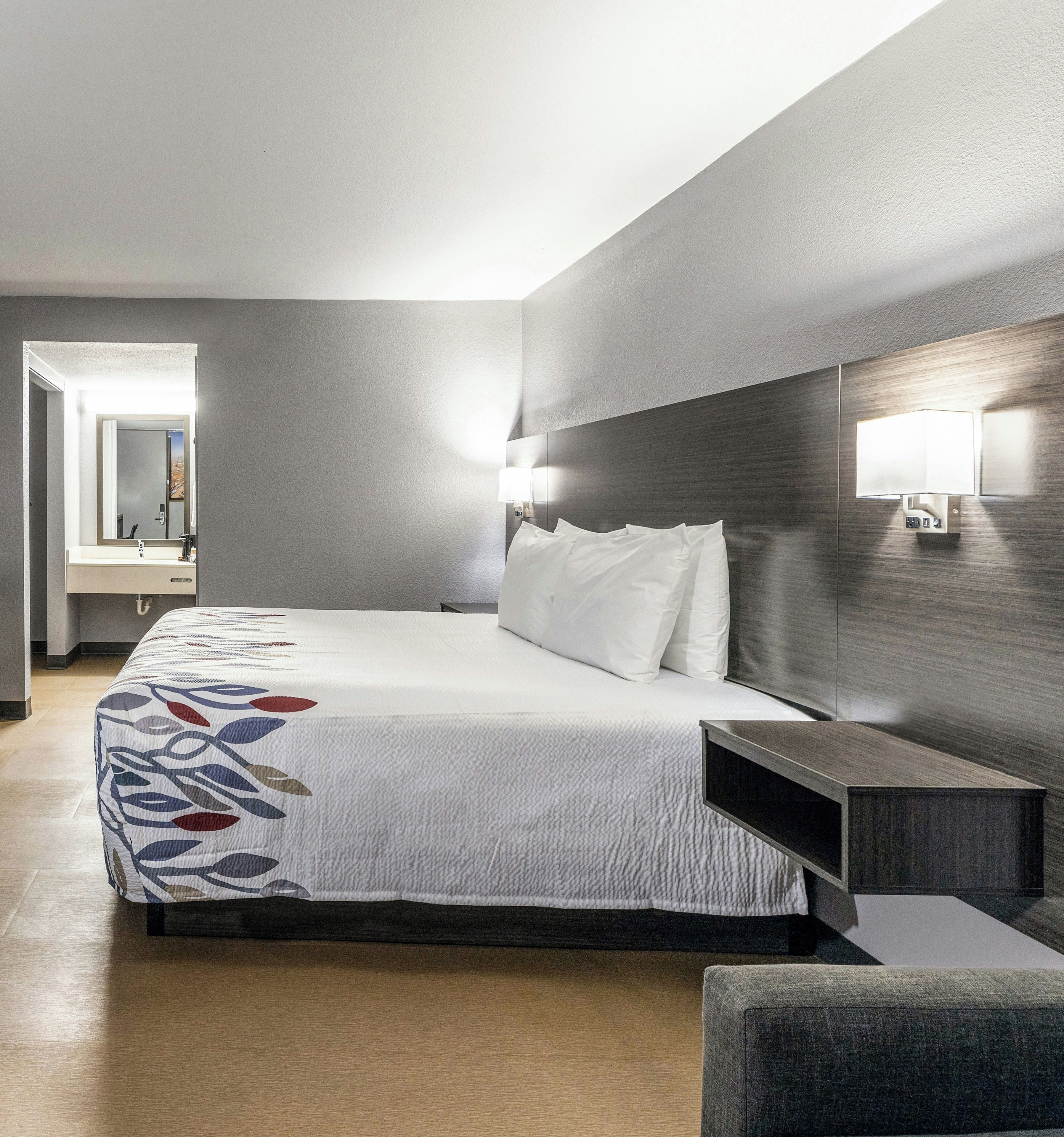 A hotel room with a bed, bedside table, lamp, and a mirror.