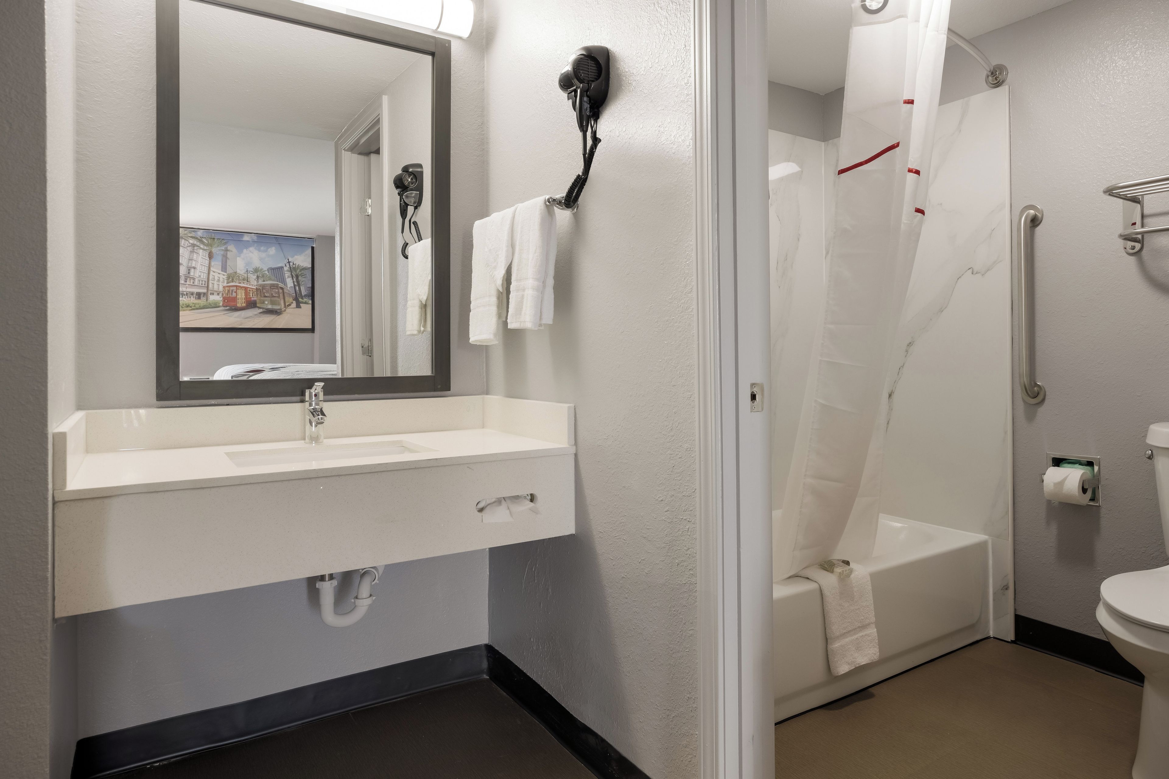 A bathroom with a sink, mirror, hair dryer, shower, and toilet.