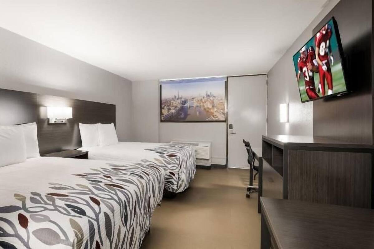 A hotel room with two beds, a TV, a desk, and a cityscape view.