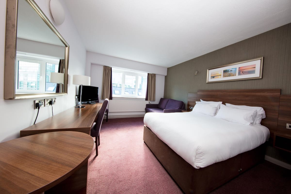 A hotel room with a bed, a desk, a chair, a television, and a window.