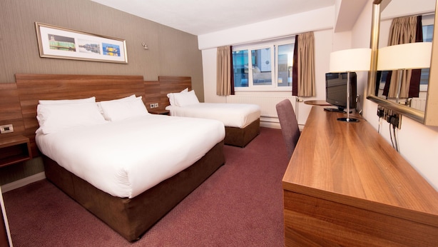 A hotel room with two beds, a desk, a TV, and a window with curtains. - Leonardo Hotel Cork (Cork)