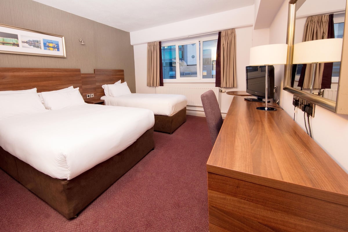 A hotel room with two beds, a desk, a TV, and a window with curtains.