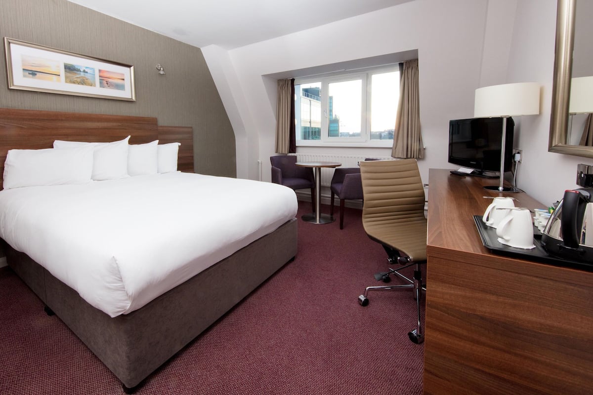 A hotel room with a large bed, a desk with a chair, a television, and a window with curtains.