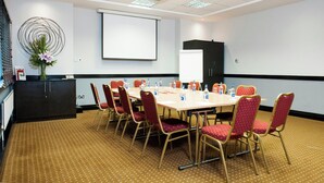 A conference room with a long table, red chairs, a projector screen, and a decorative wall piece. - Leonardo Hotel Cork (Cork)