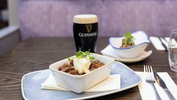 A bowl of stew with a garnish on a plate, a glass of Guinness beer, and a bowl of soup on a table.