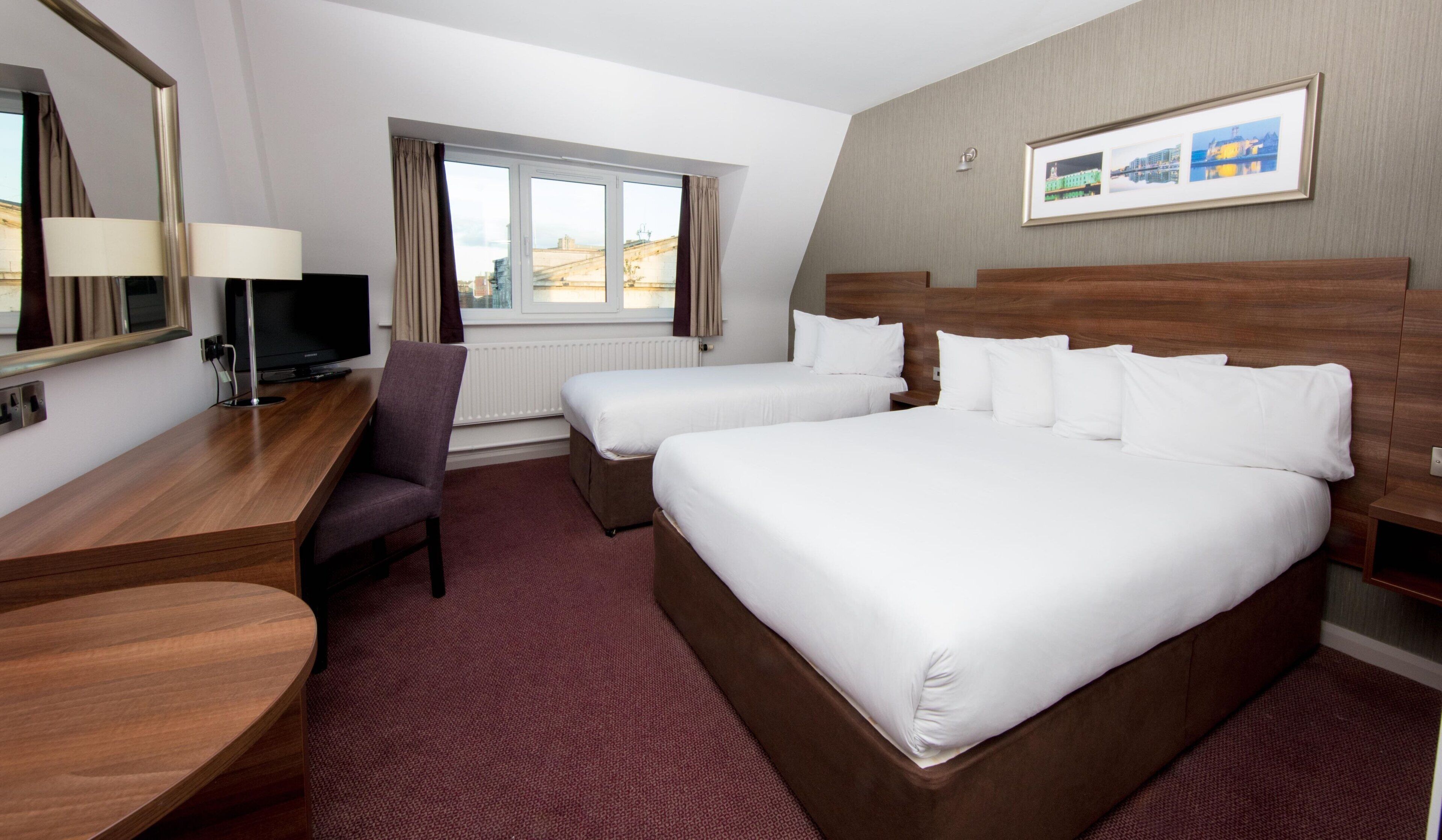 A hotel room with a large bed, a desk, a chair, a TV, and a window with curtains.
