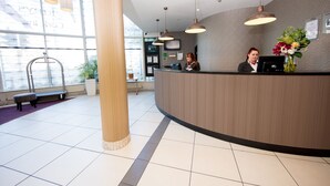A reception desk with a wooden finish, a large window with a view, and a bench in the foreground. - Leonardo Hotel Cork (Cork)