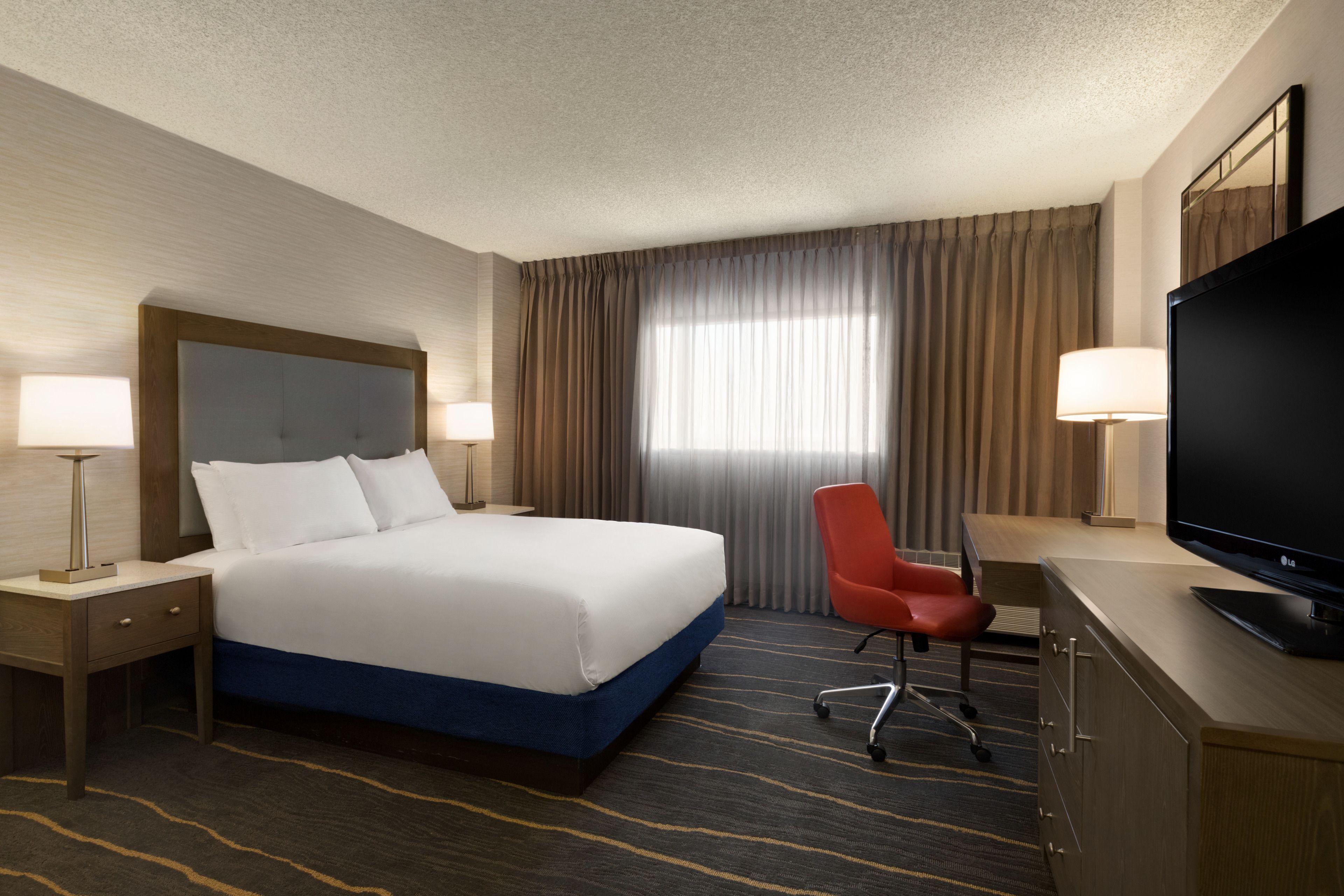 Une chambre d’hôtel avec un grand lit, un bureau avec une télévision, une chaise et deux lampes de chevet.