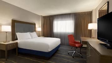 A hotel room with a large bed, a desk with a TV, a chair, and two bedside lamps.