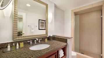 A hotel bathroom with a granite countertop sink, a large mirror, a framed picture, and a shower area.