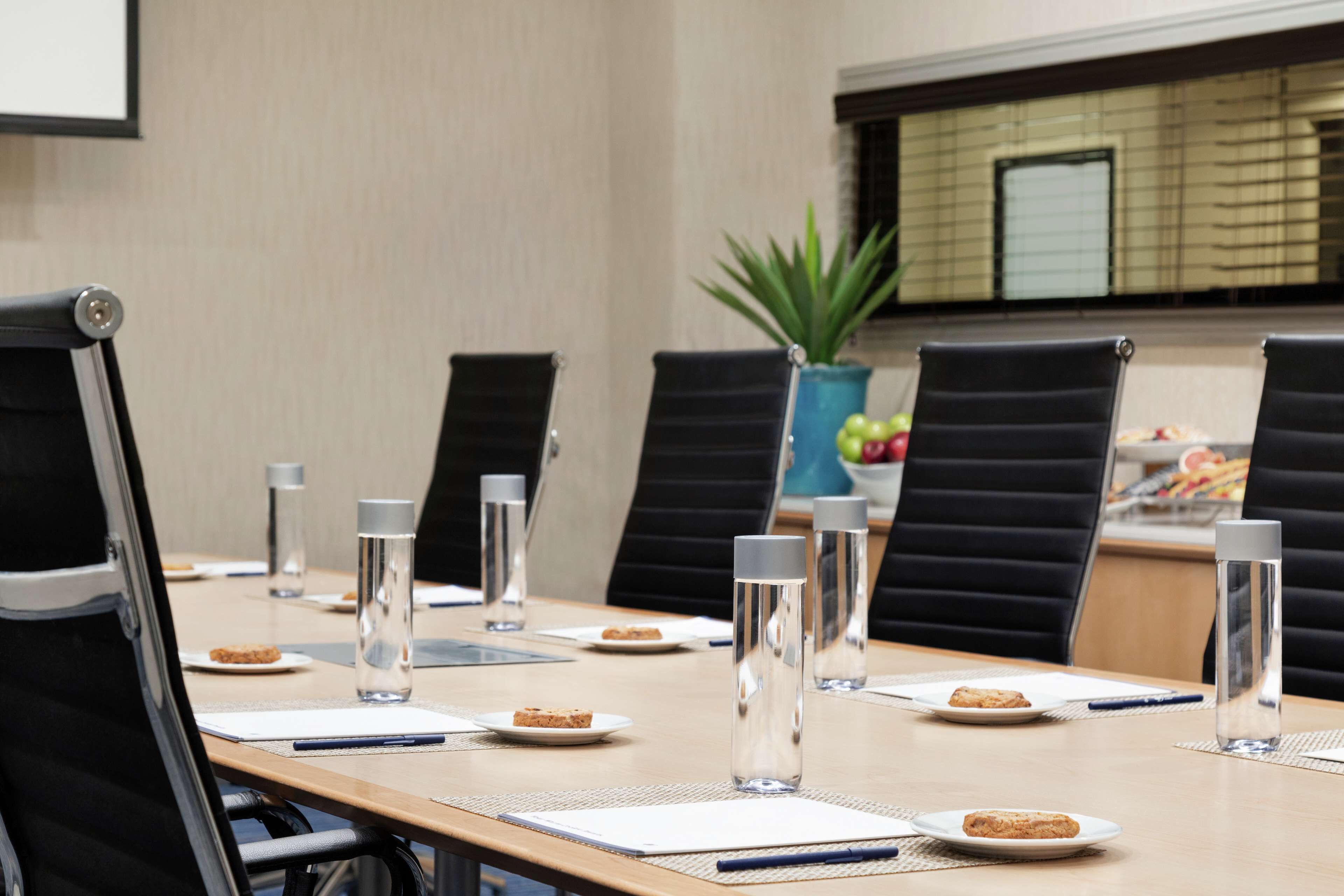 A conference room with a long table, black chairs, water bottles, and plates with food.