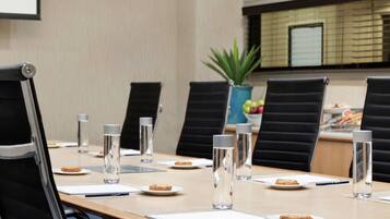 A conference room with a long table, black chairs, water bottles, and plates with food.