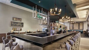 Un espace bar moderne doté d’un îlot central, de tabourets de bar, de luminaires suspendus et d’œuvres d’art accrochées aux murs.
