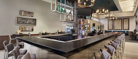 A modern bar area with a central island, bar stools, hanging lights, and artwork on the walls.