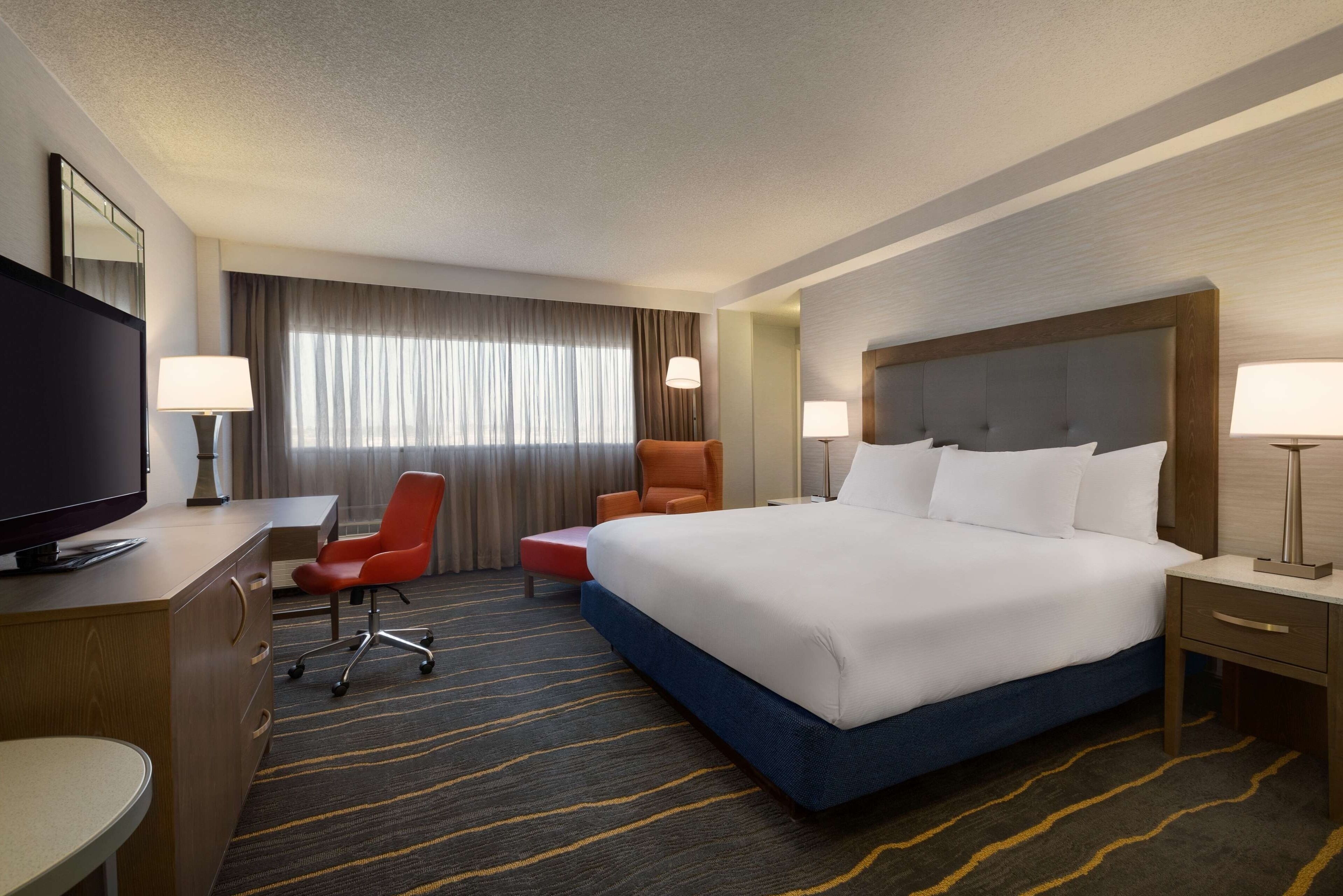 Une chambre d’hôtel avec un grand lit, un bureau avec une télévision, une chaise et une lampe de bureau.