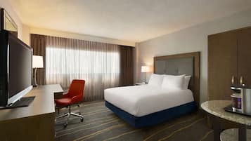 Habitación de hotel con una cama, un escritorio con computadora, una silla roja, una mesita redonda y un televisor.