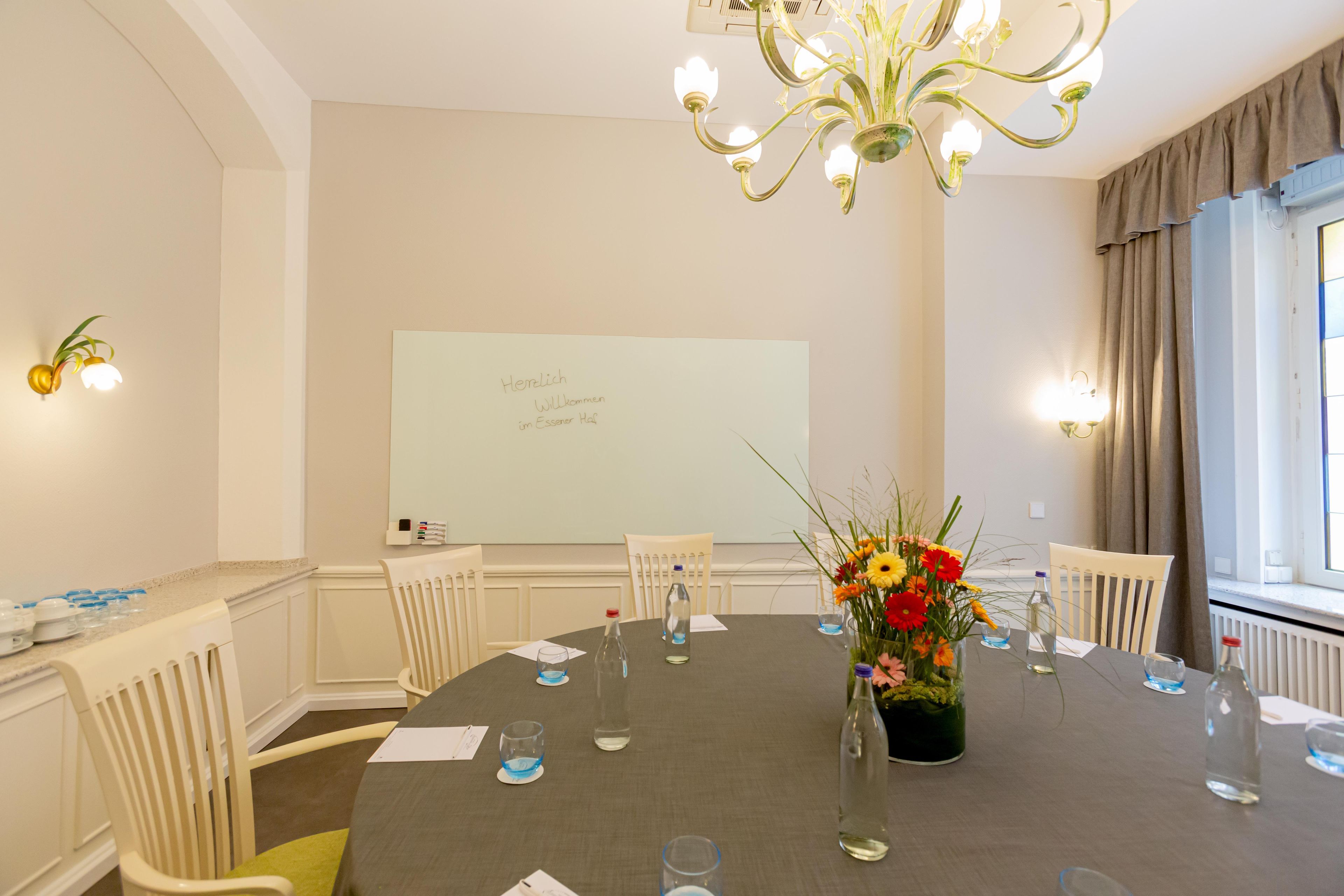 A conference room with a round table, chairs, a whiteboard, and a floral centerpiece.