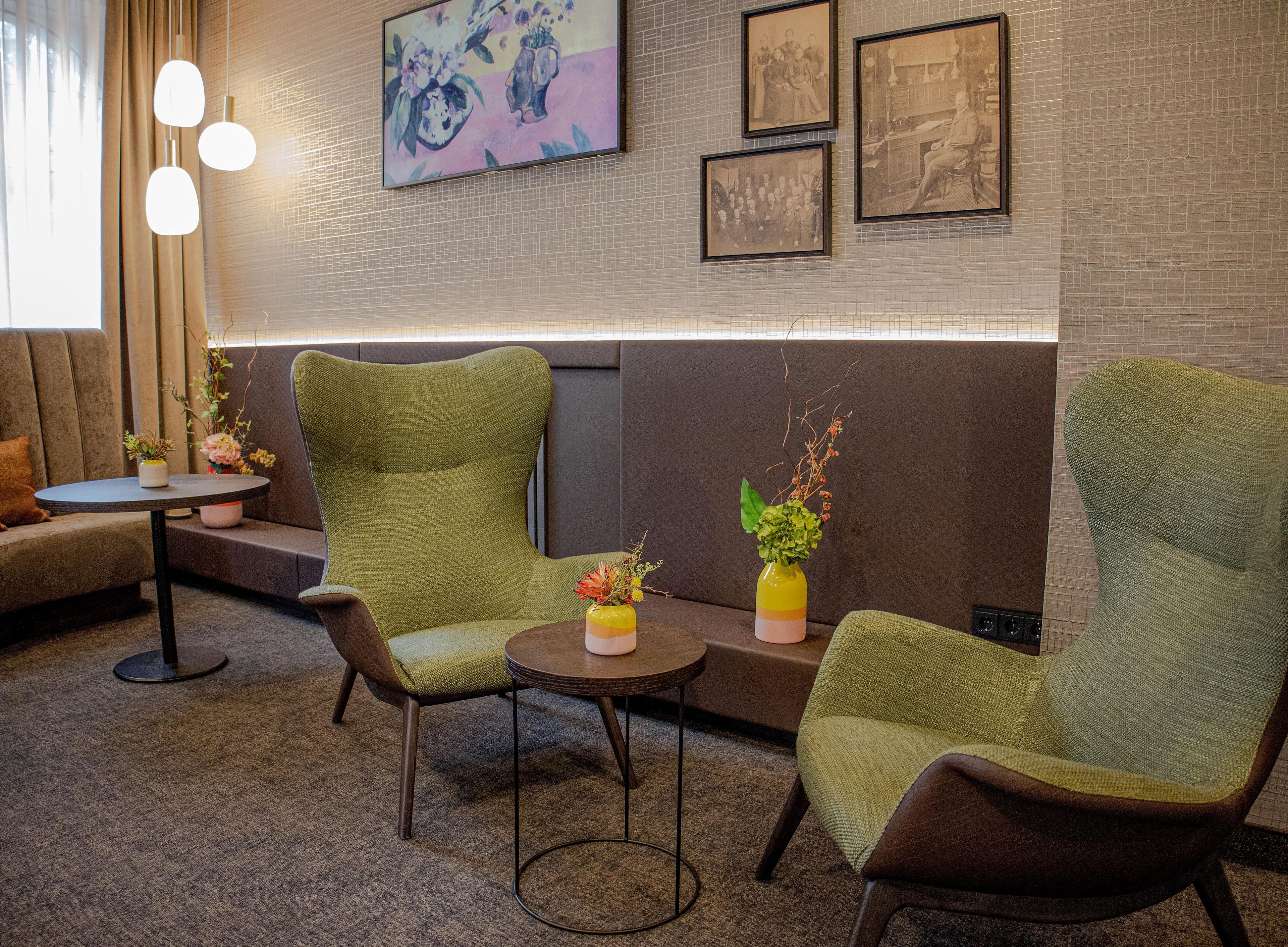 A modern lounge area with green upholstered chairs, a small round table, and a vase with flowers.