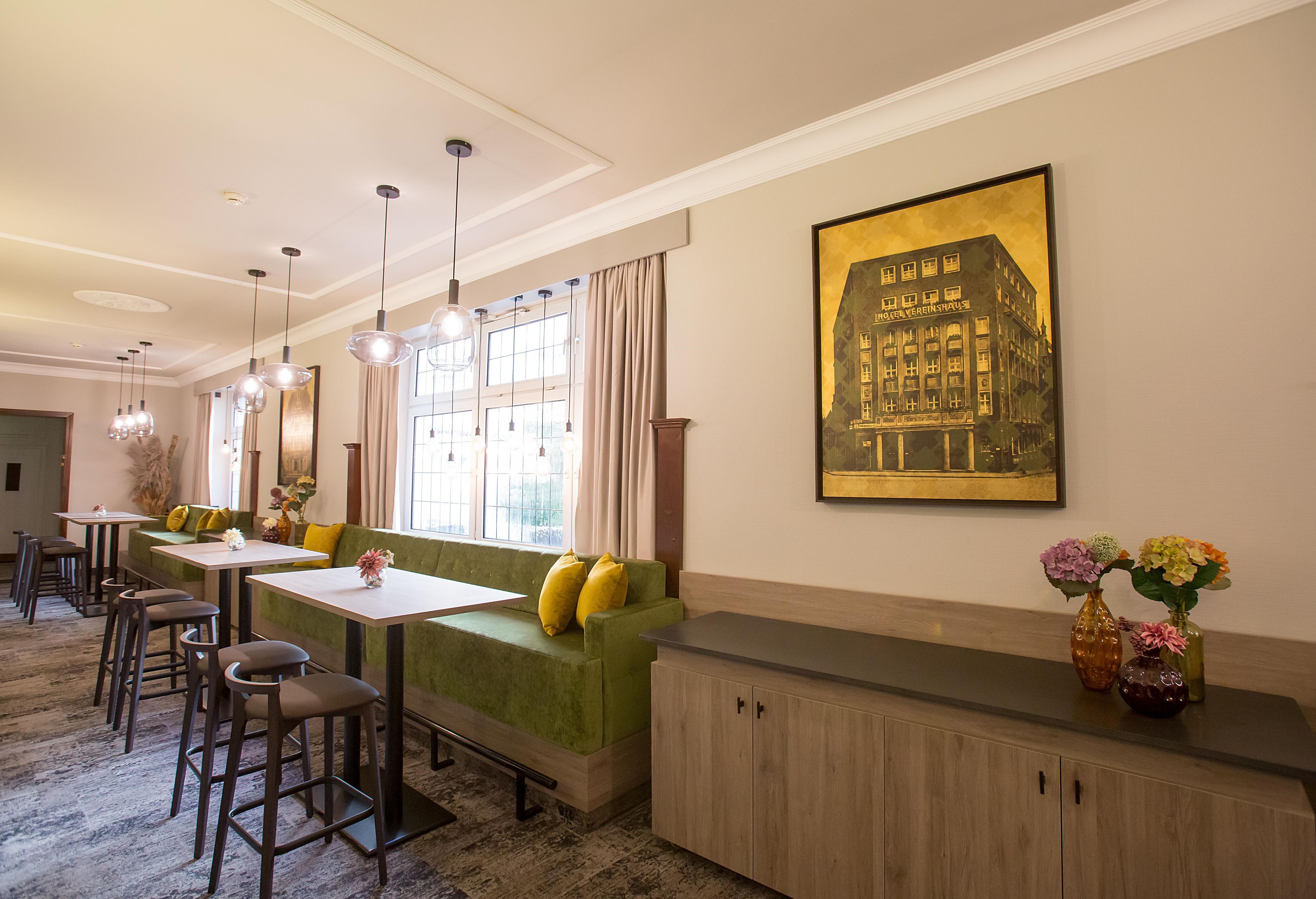 Un comedor de hotel con un sofá verde, varias mesas y lámparas colgantes.