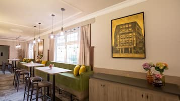 Un comedor de hotel con un sofá verde, varias mesas y lámparas colgantes.