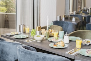 Desayuno con platos de comida, un bol de fruta, un vaso de jugo de naranja y un dispensador de azúcar.