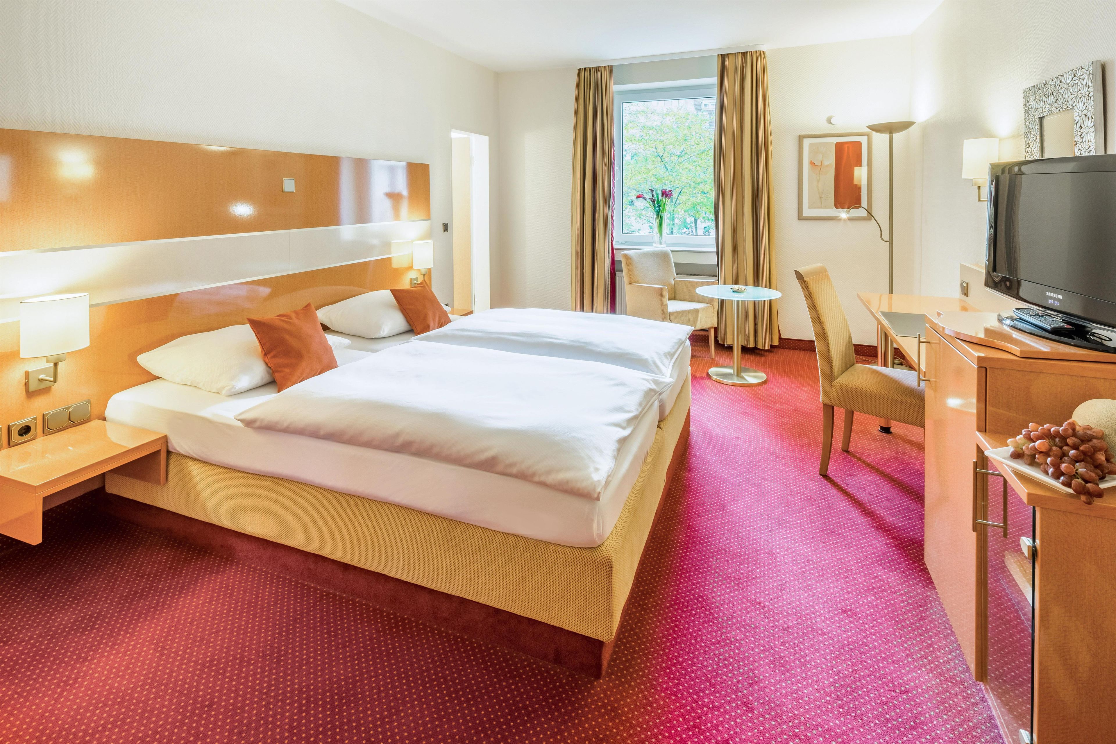 Une chambre d’hôtel avec un grand lit, un bureau avec une télévision et une chaise.