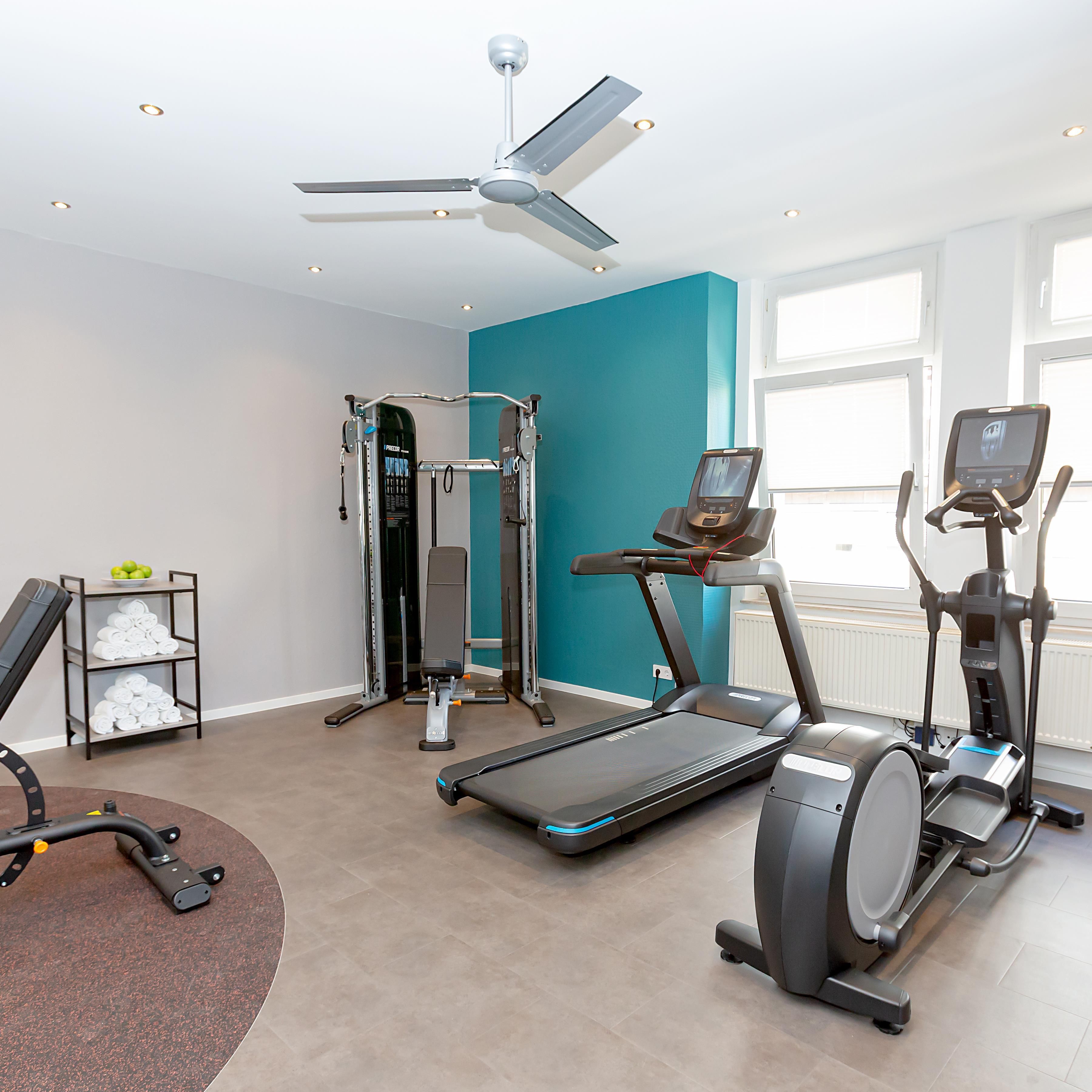 A home gym with a ceiling fan, a treadmill, an elliptical, a weight machine, and a wall-mounted TV.