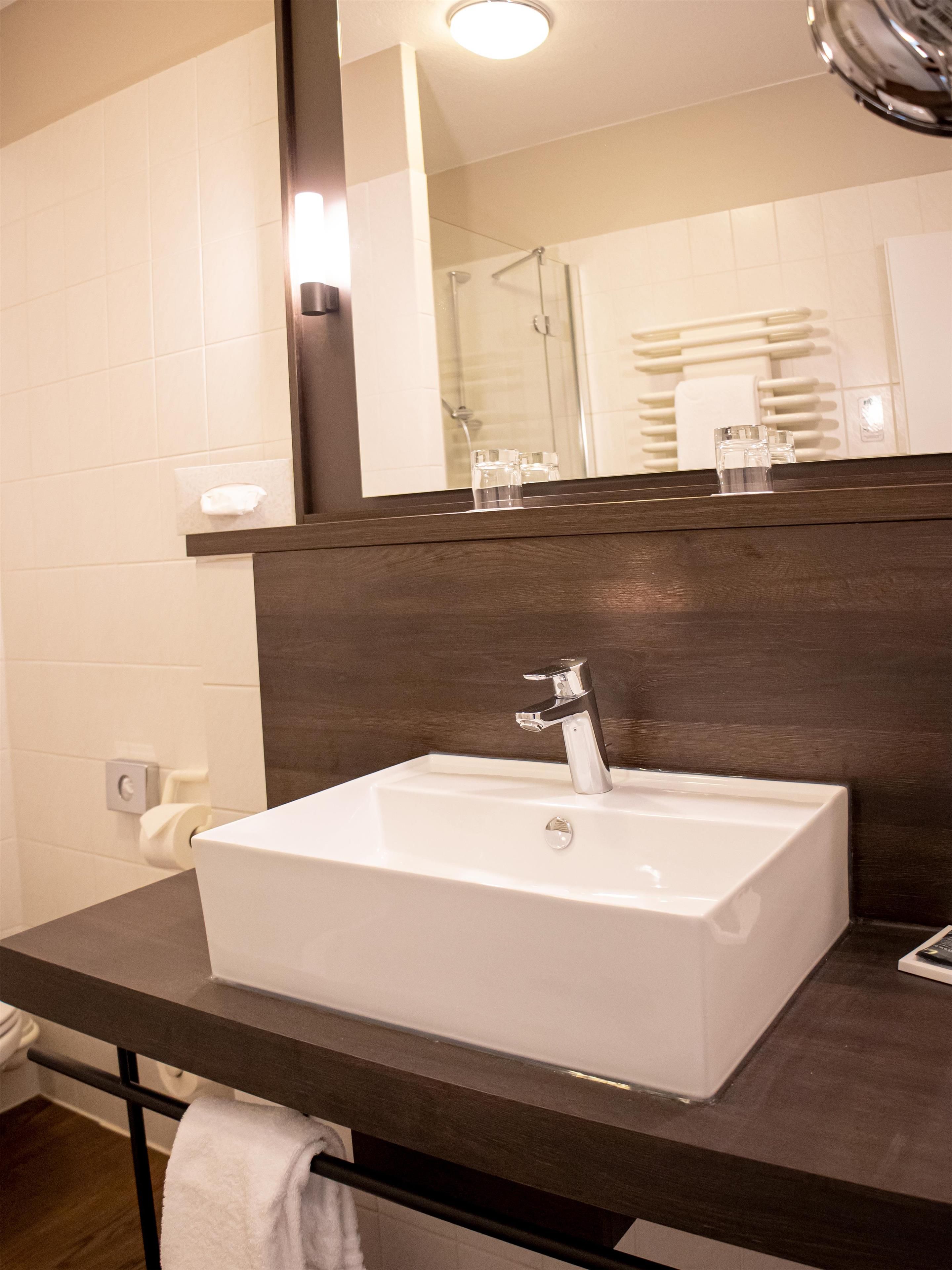 A bathroom with a white sink, dark countertop, and a mirror above it.