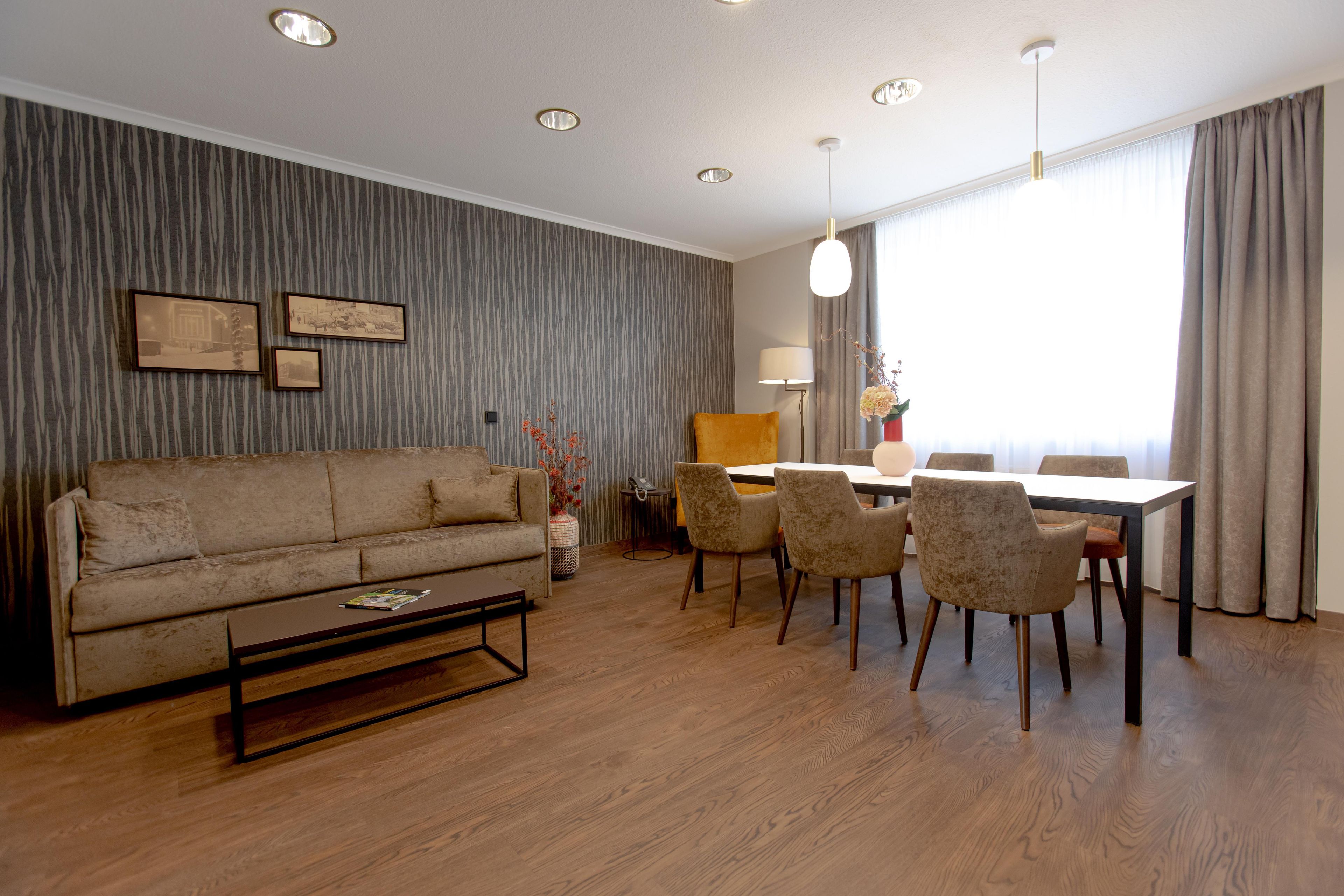 Ein modernes Wohnzimmer mit einer Couch, einem Couchtisch, einem Esstisch, Stühlen und einer Lampe.