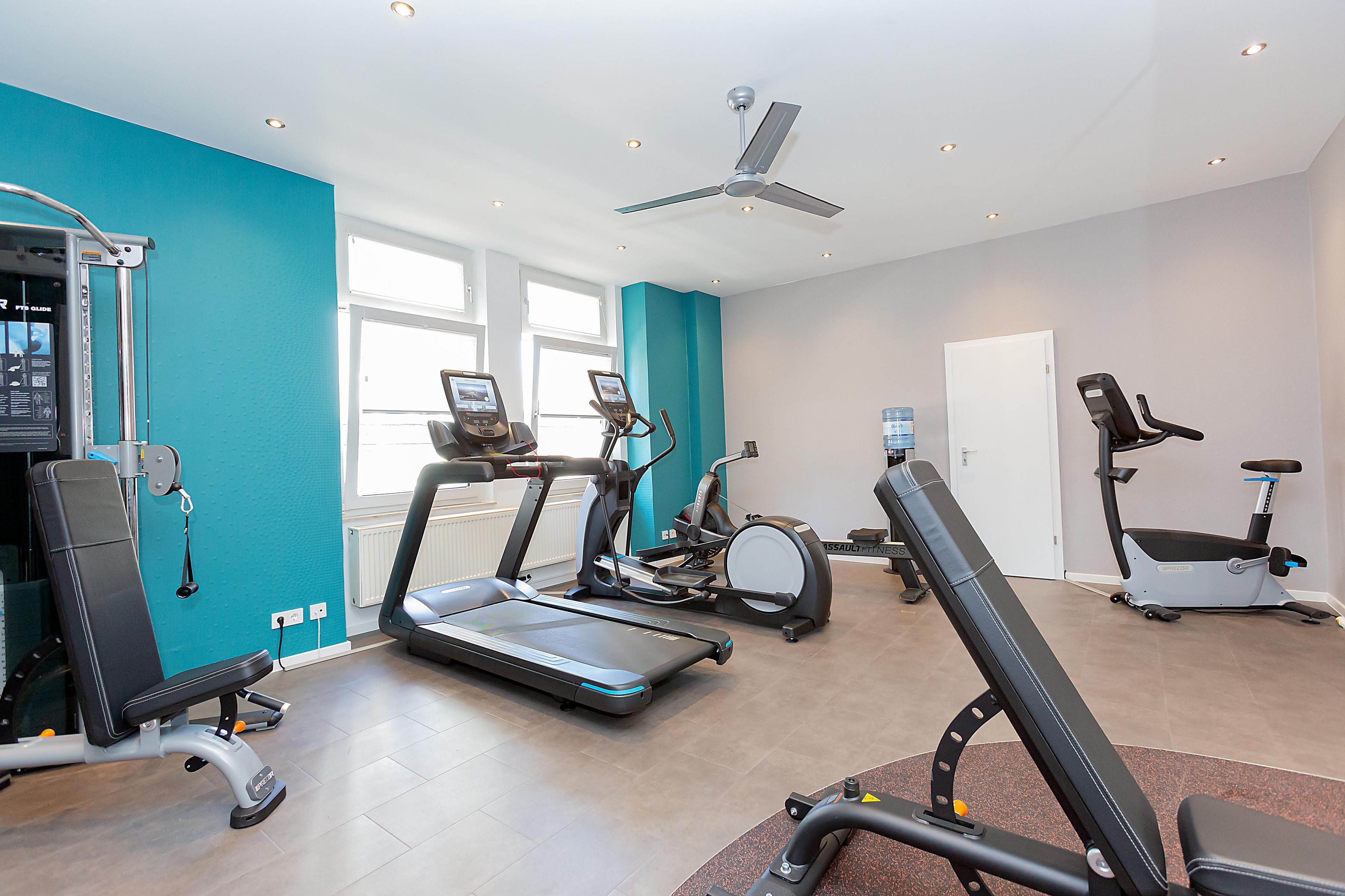 Ein Fitnessstudio mit verschiedenen Trainingsgeräten, darunter Laufbänder, ein Crosstrainer und ein Rudergerät.