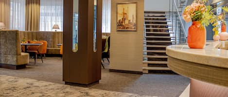 Un hall d’hôtel comprenant un comptoir d’accueil, un espace salon, un escalier et un grand tableau encadré accroché au mur.