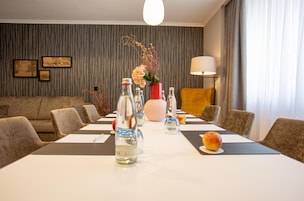 Habitación de hotel con una mesa de comedor para seis personas, un sofá, una lámpara y cuadros en la pared.