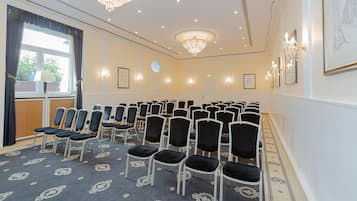 Ein Konferenzraum mit Stuhlreihen, einem Chandelier, gerahmten Kunstwerken und einem Fenster mit Vorhängen.