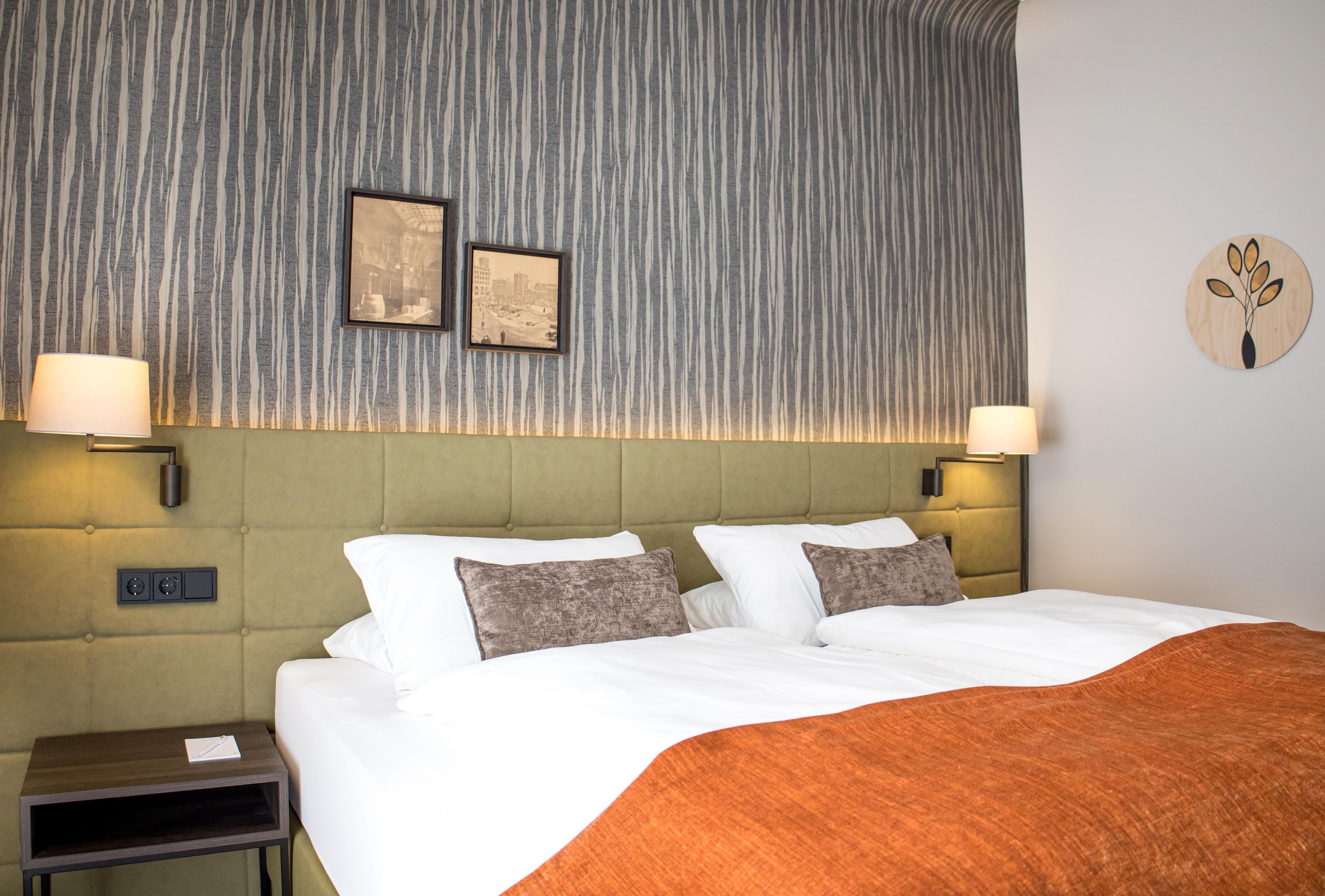 A hotel room with a large bed, two wall-mounted lamps, a framed picture, a nightstand, and a round wall decoration.