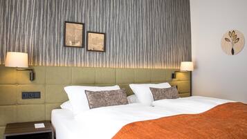 A hotel room with a large bed, two wall-mounted lamps, a framed picture, a nightstand, and a round wall decoration.