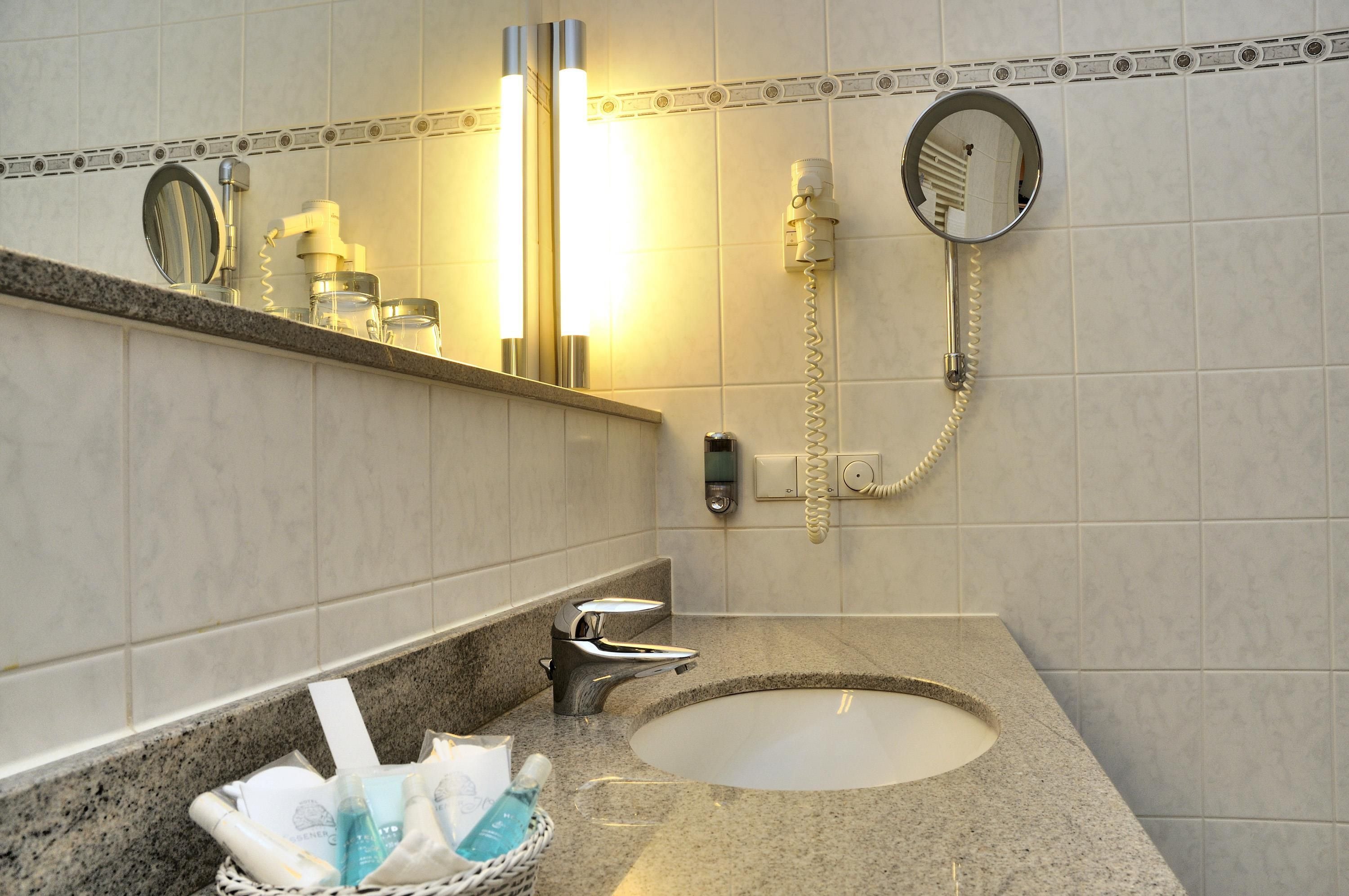 A bathroom with a sink, mirror, and a hairdryer mounted on the wall.