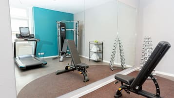 Un gimnasio con equipo de ejercicio, cinta de correr y pared con espejos.