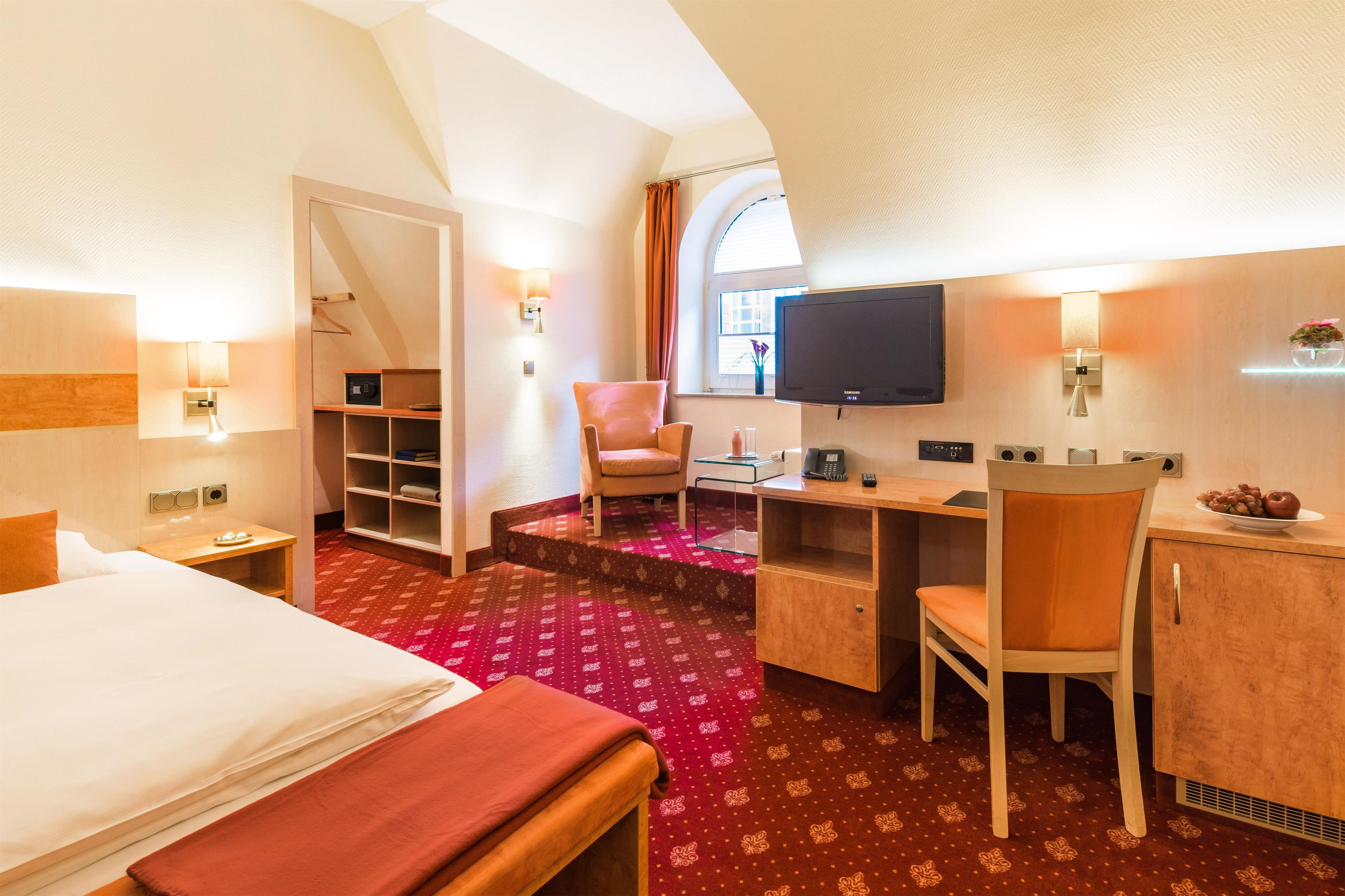 Ein Hotelzimmer mit Bett, Schreibtisch, Stuhl, Fernseher und einem kleinen Tisch mit einer Vase.