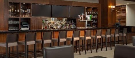 A bar area with multiple shelves of bottles and glasses, bar stools, and a table with chairs.