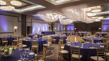A banquet hall with round tables, blue tablecloths, and gold chairs.