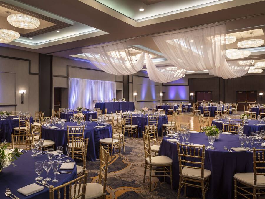 A banquet hall with round tables, blue tablecloths, and gold chairs.