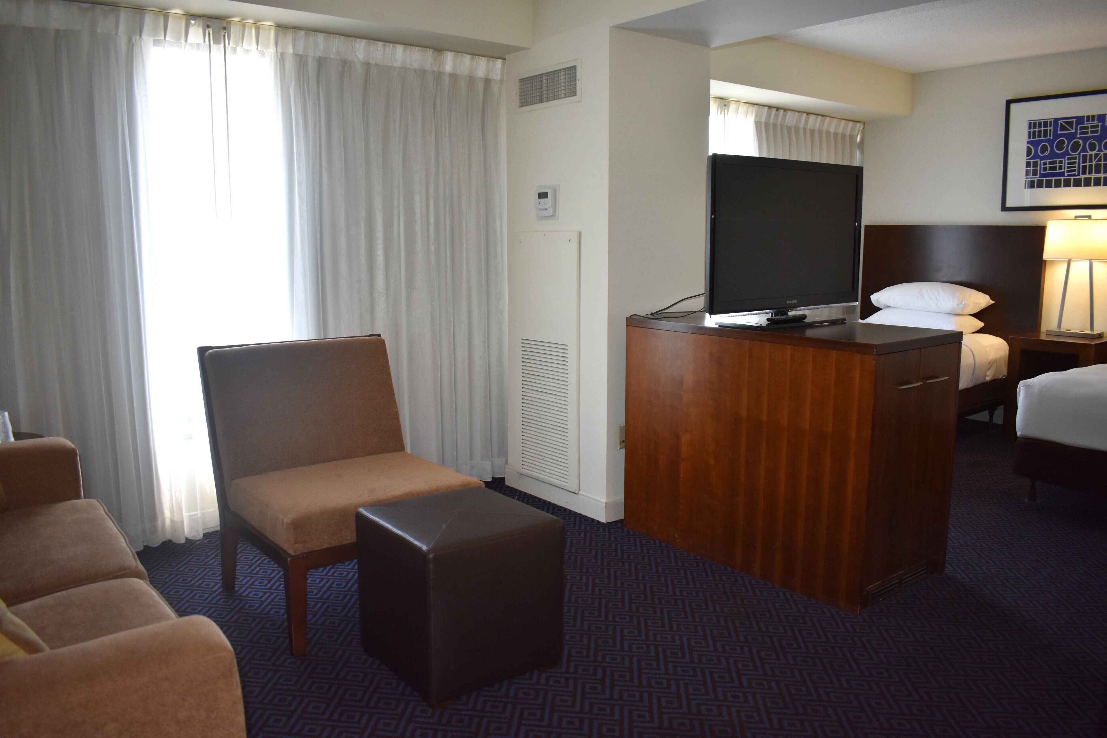 Ein Hotelzimmer mit einem Bett, einem Schreibtisch mit Fernseher, einem Sessel und einem kleinen Tisch.