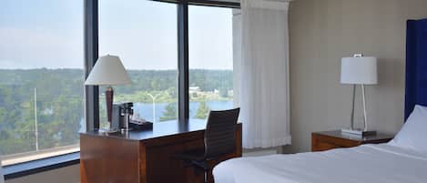 Habitación de hotel con un ventanal grande, un escritorio, una silla, una cama y dos mesitas de noche con lámparas.