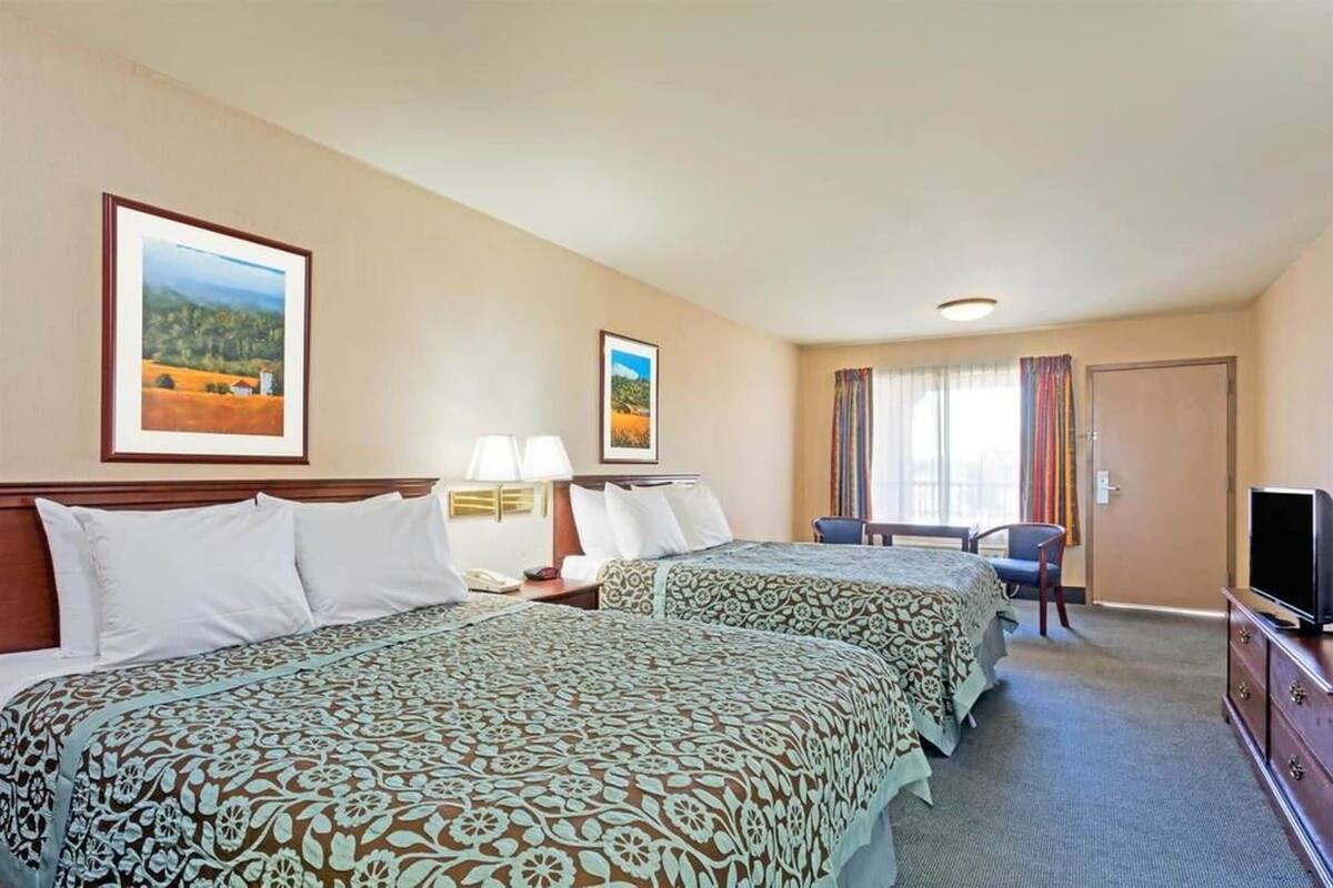 A hotel room with two beds, a desk, a chair, a television, and framed pictures on the wall.