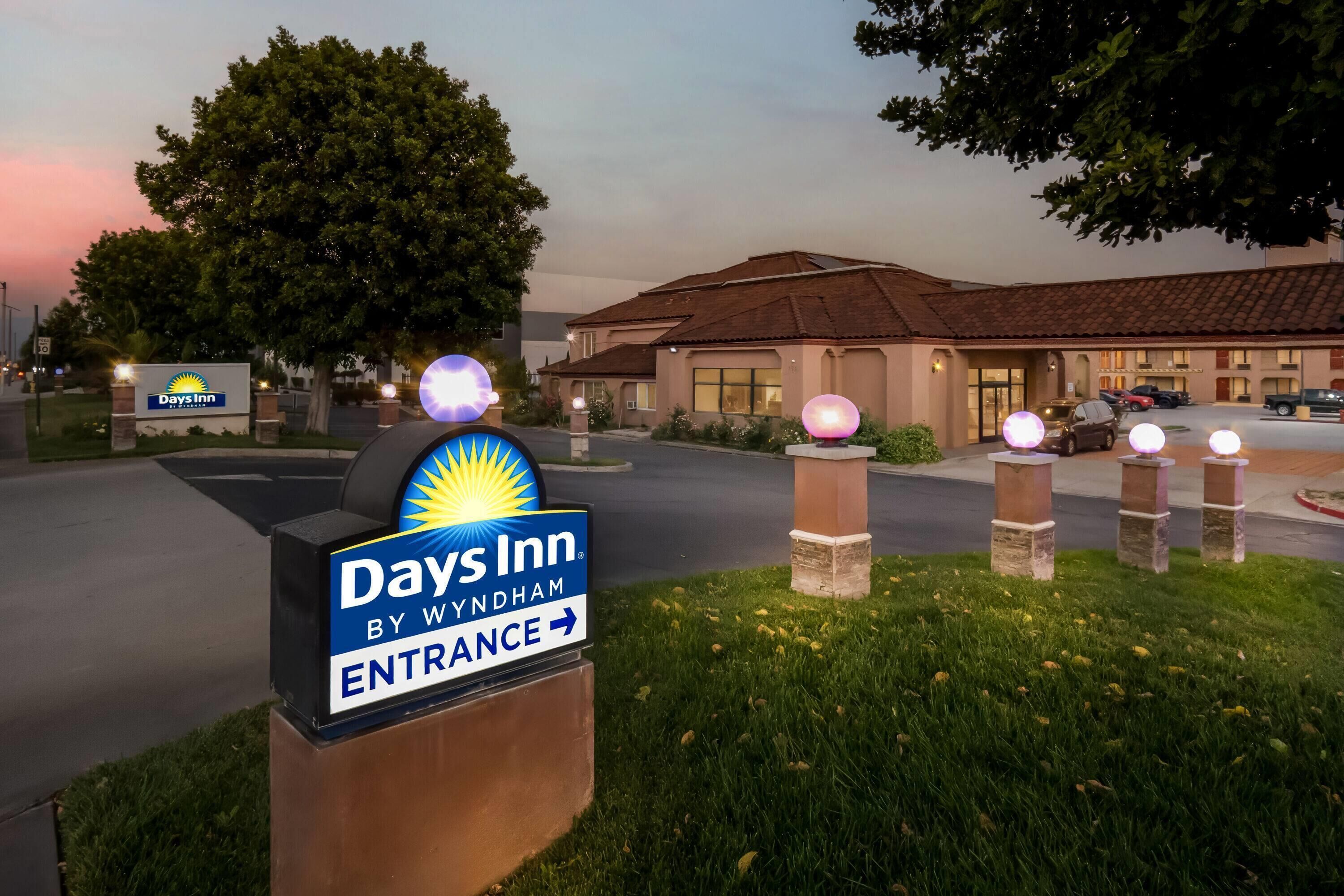 A Days Inn entrance sign with directional arrows, a parking lot, and a building with a tiled roof.