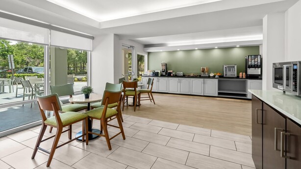A modern kitchen with white cabinets, a large window, and a dining area with green chairs. - Quality Inn Orlando Near International Drive (Orlando)