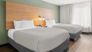 A hotel room with two beds, a wooden headboard, a nightstand, and a window with curtains. - Quality Inn Orlando Near International Drive (Orlando)
