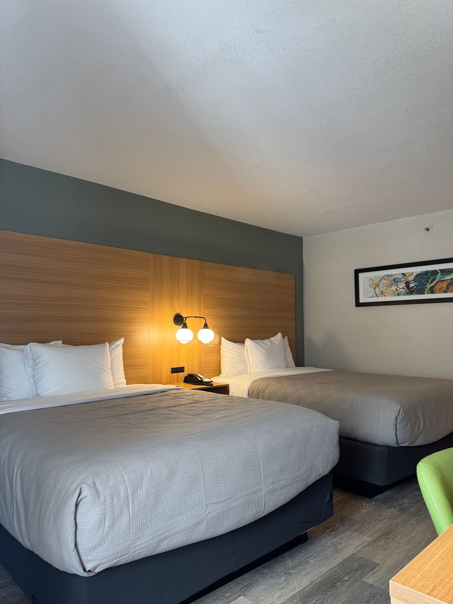 A hotel room with two beds, a wooden headboard, a wall-mounted light fixture, and a framed picture.